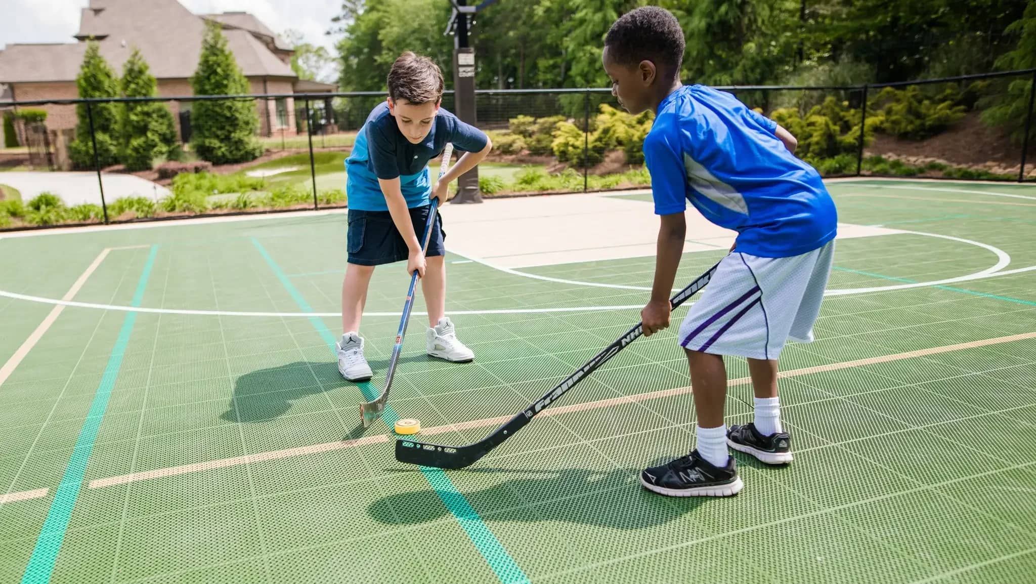 Two children playing hockey on a green Arena X300 outdoor court.